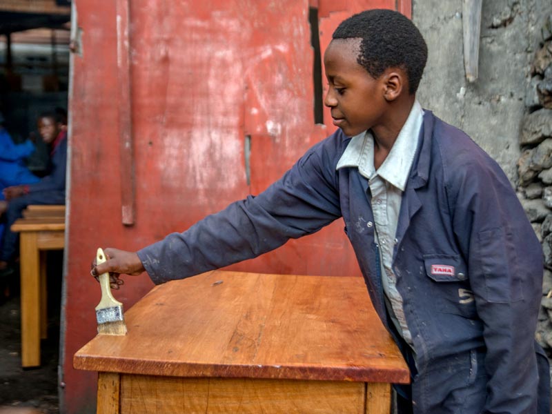 Jeune apprenti vernissant la table qu'il vient de fabriquer devant le jury du brevet de menuisier à Goma