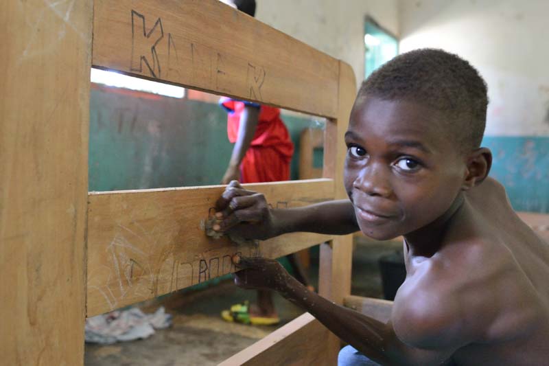 Enfant Pygmée Bagyeli effaçant les graffiti sur les lits du Fondaf Bipindi au Cameroun