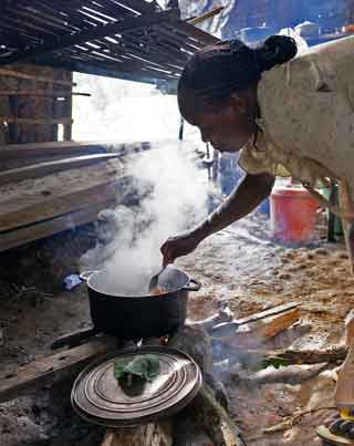 Une maman Pygmée Bagyeli prépare le repas dans une marmite sur un feu de bois dans son campement.