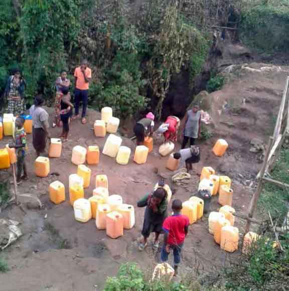 Femmes et enfants puisant de l'eau à la source dans la vallée au bas de Kitolu